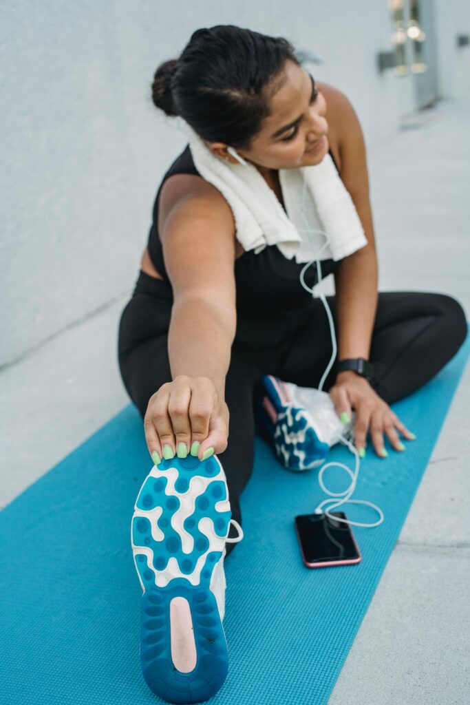 Woman enjoying a post-yoga exercise stretch on a mat while listening to music outdoors.